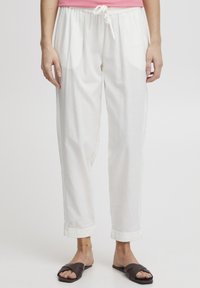 Pantalons en lin blancs avec une taille élastique, design ajusté et ourlets retroussés. Associés à des sandales plates marron.