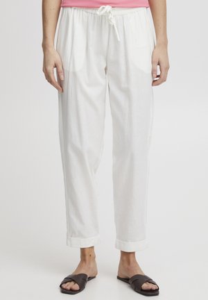 Pantalons en lin blancs avec une taille élastique, design ajusté et ourlets retroussés. Associés à des sandales plates marron.