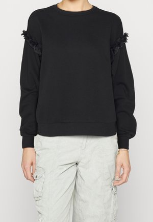 Suéter negro de manga larga con ribete floral texturizado en las mangas, combinado con pantalones cargo gris claro.