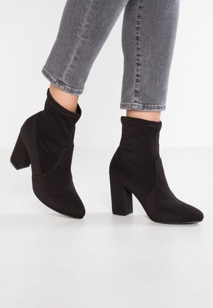 Botines negros de tacón alto hechos de suave ante. Presentan una punta puntiaguda y un tacón en bloque de altura media. El diseño incluye acentos cosidos.