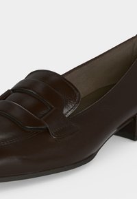 Mocassin femme en cuir marron foncé avec un petit talon bloc et une large bride sur le dessus.