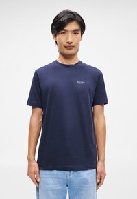 Σκούρο μπλε βαμβακερό T-shirt με κοντά μανίκια, στρογγυλή λαιμόκοψη και ένα μικρό λευκό λογότυπο στο στήθος. Μαλακή υφή, κανονική εφαρμογή.