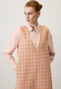 Orange and white checkered dress with a V-neck design, layered over a pink collared shirt; both have smooth textures and structured shapes.