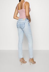 Světle modré džíny s rovného střihu a diskrétním prošíváním zadních kapes. Kombinované s růžovým upnutým topem a průhlednými sandály na podpatku.