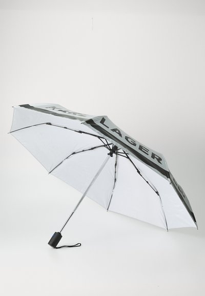 Parapluie blanc avec des accents noirs, arborant le texte "KARL LAGERFELD." Il a un mât en métal et une poignée compacte avec une sangle.