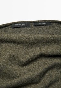 Tessuto di cashmere verde oliva scuro, con una texture morbida, etichette che riportano "Massimo Dutti" e "100% CASHMERE" visibili lungo il bordo.