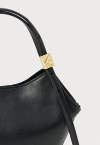 Melna ādas soma ar gludu faktūru, rotāta ar zelta aparatūru un minimālistisku formu ar vienu plecu siksnu.