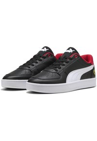 Sorte og hvide sneakers med en glat læderoverdel, net-tunge, røde accenter og hvid gummisål; har perforeringer og logo-detalje.
