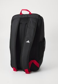 Svart ryggsekk med røde detaljer, utstyrt med polstret mesh-bak, justerbare stropper og en sidemesh-lomme. Adidas-logo på forsiden.