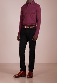 Bordeauxfarbendes Langarm-Polohemd, schwarze schmal geschnittene Jeans, brauer geflochtener Gürtel und braune Schnürstiefel mit glatter Oberfläche.
