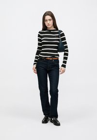 Mustvalge triibuline pikkade varrukatega top, sinised teksad, pruun vöö ja mustad kingad. Väike sinine käekott õlarihmaga.