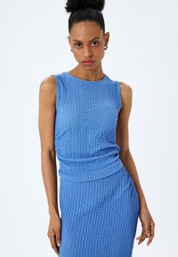 Vestido sin mangas azul con textura, de silueta ajustada, que presenta un acento fruncido en el costado y un escote redondo y suave.