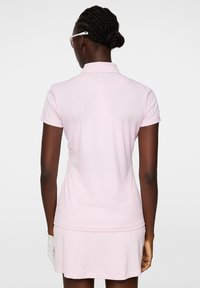 Różowa koszulka polo z krótkim rękawem, teksturowana tkanina, subtelne logo z tyłu, w zestawie z pasującą różową spódnicą.