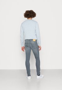 Sudadera de textura azul clara, con cuello redondo, combinada con jeans ajustados grises que tienen un parche amarillo en el bolsillo trasero. Se llevan zapatillas blancas.