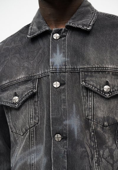 Σκούρο γκρι μπουφάν denim με ασημένια κουμπιά χαραγμένα με σταυρό, δύο τσέπες στο στήθος με καπάκια και διακριτικά αφηρημένα σχέδια στο ύφασμα.