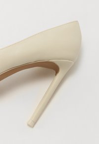 Beżowy but na wysokim obcasie z ostrym noskiem, gładką syntetyczną cholewką i smukłym obcasem typu stiletto, z brązowym wnętrzem.