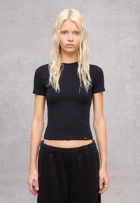 Camiseta negra ajustada de manga corta en tejido de mezcla de algodón, con cuello redondo y una pequeña etiqueta de la marca en el dobladillo inferior.