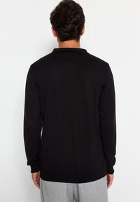 Svart långärmad polo skjorta med ribbad krage och manschetter. Slät textur och avslappnad passform. Synliga sömnadsdetaljer på sömmarna.