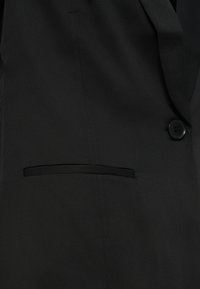 Chaqueta de traje negra con tejido texturizado, con cierre de un solo botón y un bolsillo estrecho alineado con la costura.