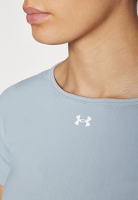 Helesinine istuv särk, millel on ümmargune kaelus ja lühikesed varrukad. Valge Under Armour'i logo asub vasakul rinnakorvil.