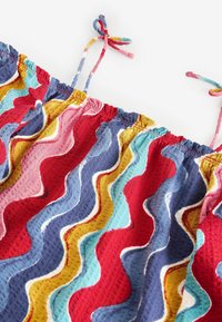 Tissu coloré à motifs ondulés présentant des teintes rouges, bleues, jaunes et roses. Encolure froncée avec des attaches. Surface texturée.