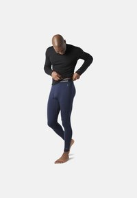 Marina termobyxor och en svart långärmad topp, tillverkad av ett stretchigt tyg. Midjan har varumärket "smartwool" i vitt.