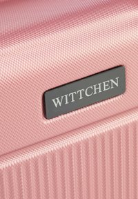 Pink hard-shell suitcase with a textured surface, featuring vertical ridges and a black brand tag reading "WITTCHEN." Smooth finish.