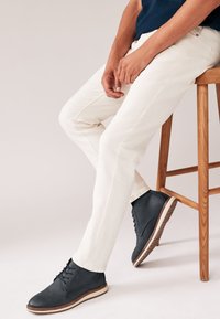 Light beige pants made of cotton with a slim fit and minimal stitching, paired with dark navy leather shoes featuring a white sole.