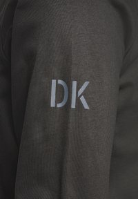 Black textured fabric long-sleeve shirt with a gray "DK" logo printed on the left sleeve. The design is simple and modern.