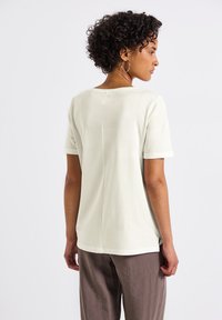 T-shirt de couleur claire, à manches courtes, avec une coupe décontractée, dotée d'un col rond, d'échancrures sur les côtés et d'une texture en coton lisse.