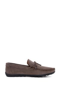 Mocasín de ante gris con suela plana de goma negra, detalle de costuras y un cordón de cuero en la parte delantera. Textura suave.