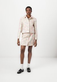 Strukturierte, pastellfarbene Jacke mit Blumenmuster und großen Knöpfen, kombiniert mit einem passenden Minirock. Schwarze Schuhe und weiße Socken runden den Look ab.