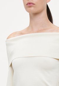 Off-shoulder kremetop med ribbet tekstur; har bred halsutskjæring. Glatt stoff og tettsittende silhuett.