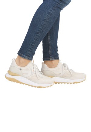 Baskets en mesh beige légères avec une semelle blanche, des accents jaunes et des lacets, portées sur des pieds dans un jean en denim bleu.