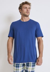 T-shirt blu a maniche corte realizzato in tessuto morbido con scollatura rotonda, abbinato a pantaloni corti a quadri caratterizzati dai colori blu, verde e bianco.