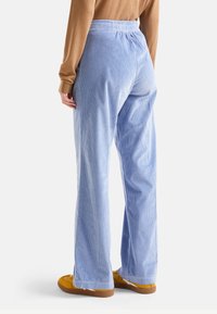 Jasnoniebieskie spodnie z kordówki o luźnym kroju, z elastycznym pasem i delikatną teksturą prążkowaną. W połączeniu z żółtymi butami.