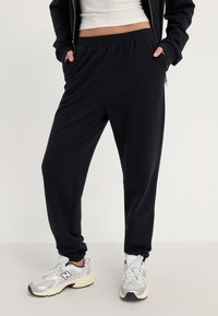 Svarte joggebukser med elastisk midjebånd og sidelommer, laget av mykt stoff. Kombinert med grå og hvite joggesko.