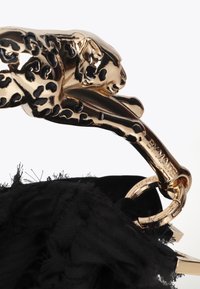 Čierna zamatová taška s zlatým klipom v tvare leopardu, ozdobená textúrovaným povrchom a strapcovými detailmi. Logo vyryté na kovových prvkoch.