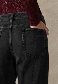 Jean en denim noir avec taille haute, conception à cinq poches et coutures contrastées. Tissu texturé légèrement délavé avec coutures visibles.