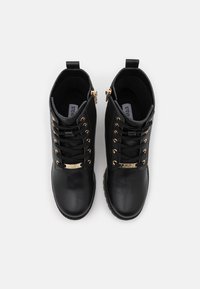 Bottines en cuir noir avec quincaillerie dorée, design à lacets et fermetures éclair sur le côté. Texture lisse avec une pointe ronde et une semelle robuste.