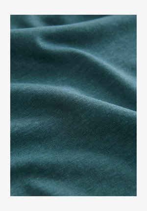 Teal színű pamutanyag, amely lágy textúrával rendelkezik, sima, hullámos redőkkel és diszkrét fényességgel, kiemelve könnyed és lélegző tulajdonságait.