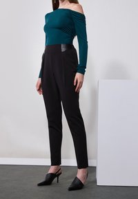 Teal off-the-shoulder top with ruched sides paired with black tailored pants featuring faux leather accents and pointed black mules.
