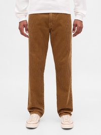 Καφέ παντελόνι κοτλέ, συνδυασμένο με λευκά αθλητικά παπούτσια και λευκό πουκάμισο με μακριά μανίκια, εμφανιζόμενο από τη μέση έως τα πόδια, σε απλό φόντο.