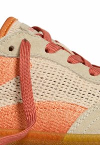 Zapatillas de deporte con cordones, que presentan una mezcla de texturas de malla y ante, predominantemente beige con acentos en naranja y una suela de goma transparente.