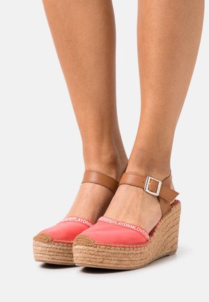 Sandales compensées en tissu corail avec brides de cheville marron, détails en jute tissé et accents de logo blanc sur la partie supérieure.