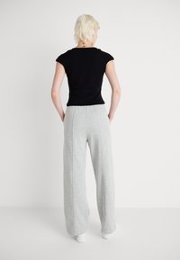Schwarzes, eng anliegendes T-Shirt mit kurzen Ärmeln, kombiniert mit hellgrauen, weiten, strukturierten Jogginghosen. Einfaches, lässiges Design mit klaren Linien.