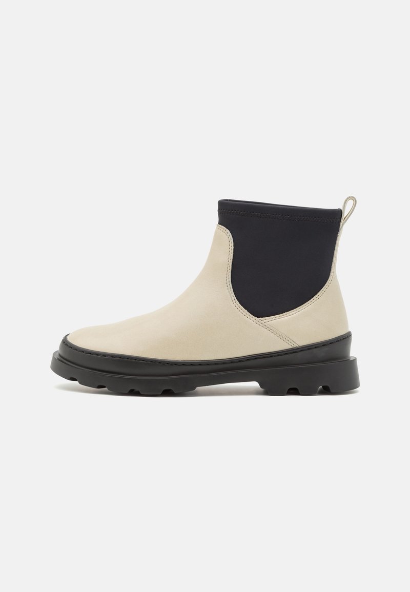 Bottine beige et noire avec une semelle noire épaisse et un languette tirette, présentant l'avant beige lisse et un tissu noir extensible autour de la cheville.