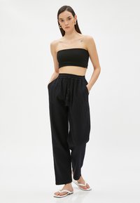 Svart ribbade bandeau-topp med lösa svarta byxor som har elastisk midja och sidofickor. Modellen bär vita flip-flops.