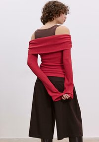 Gerippte schulterfreie Oberteil in Rot mit langen Ärmeln. Kombiniert mit braunen Culottes, die eine lockere Passform und glatte Textur aufweisen.