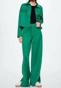 Zielony dwuczęściowy zestaw składający się z krótkiej kurtki zapinanej na guziki z dwiema kieszeniami oraz spodni o szerokich nogawkach, wykonanych z gładkiego materiału. Akcentowany złotymi guzikami.
